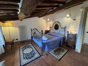 A bedroom with a bed, two rugs, a chair, a radiator, and a wooden cabinet. - Casa Max by Interhome (Capannori)