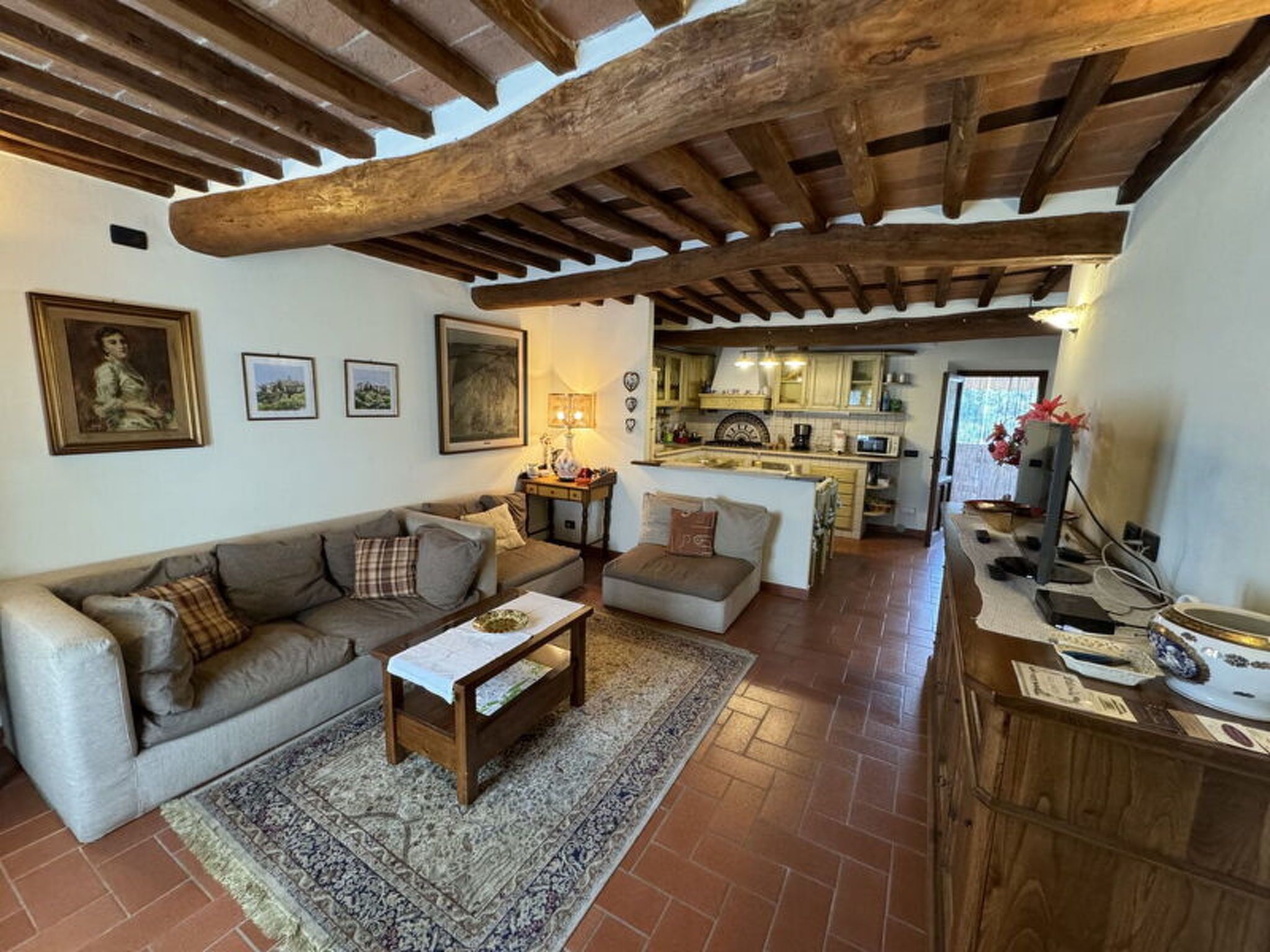 Un salon avec un canapé, une table basse et un tapis, une cuisine à l’arrière-plan et un plafond en bois.