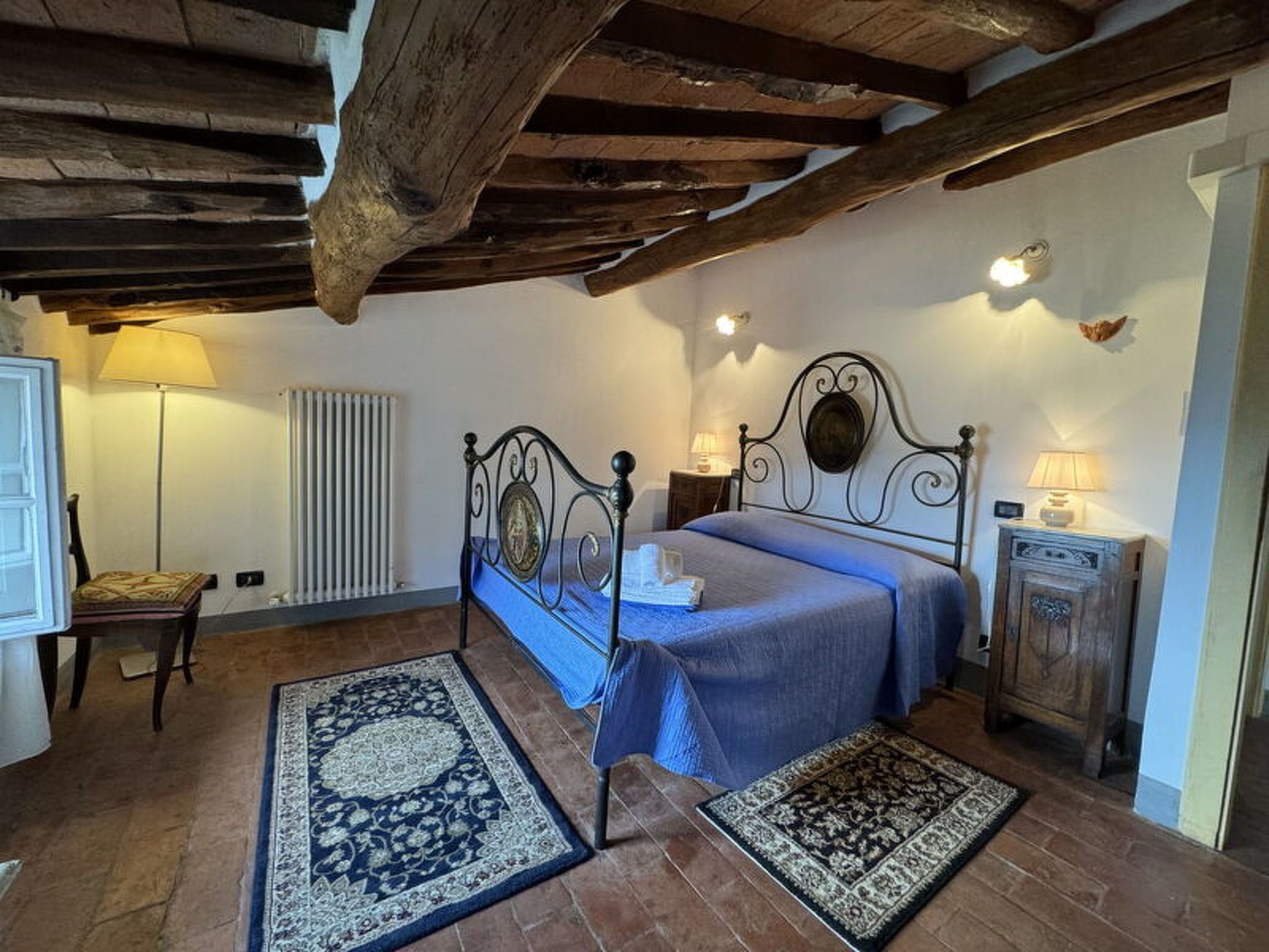 A bedroom with a bed, two rugs, a radiator, a lamp, and a wooden cabinet.