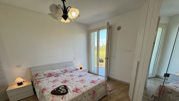 Une chambre à coucher comprenant un lit, des tables de chevet, un luminaire au plafond et une porte-fenêtre coulissante donnant sur un balcon.
