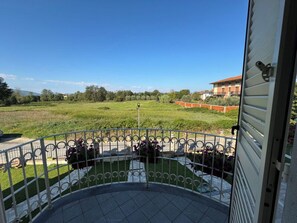 A balcony with a metal railing, a tiled floor, and a view of a green field and buildings in the distance. - Villa al Glicine by Interhome (Altopascio)