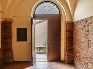 An arched doorway leading to a courtyard with a brick wall and a tiled floor. - Bocelli by Interhome (Peccioli)