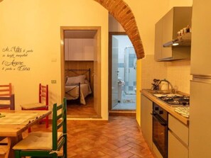 Eine kompakte Küche mit Essbereich, ein kleines Schlafzimmer mit Bett und ein durch einen Bogen erreichbares Badezimmer.