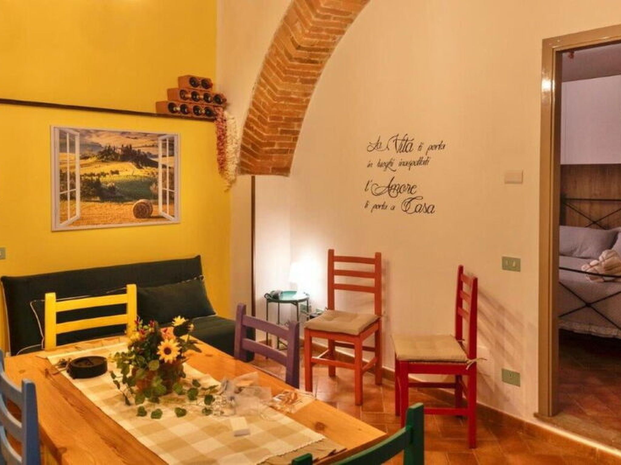 Een gezellige kamer met een houten eettafel, een groene bank en een muurschildering met een citaat.