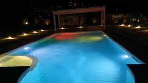 Una piscina de nit amb vores il·luminades i una zona coberta al fons.