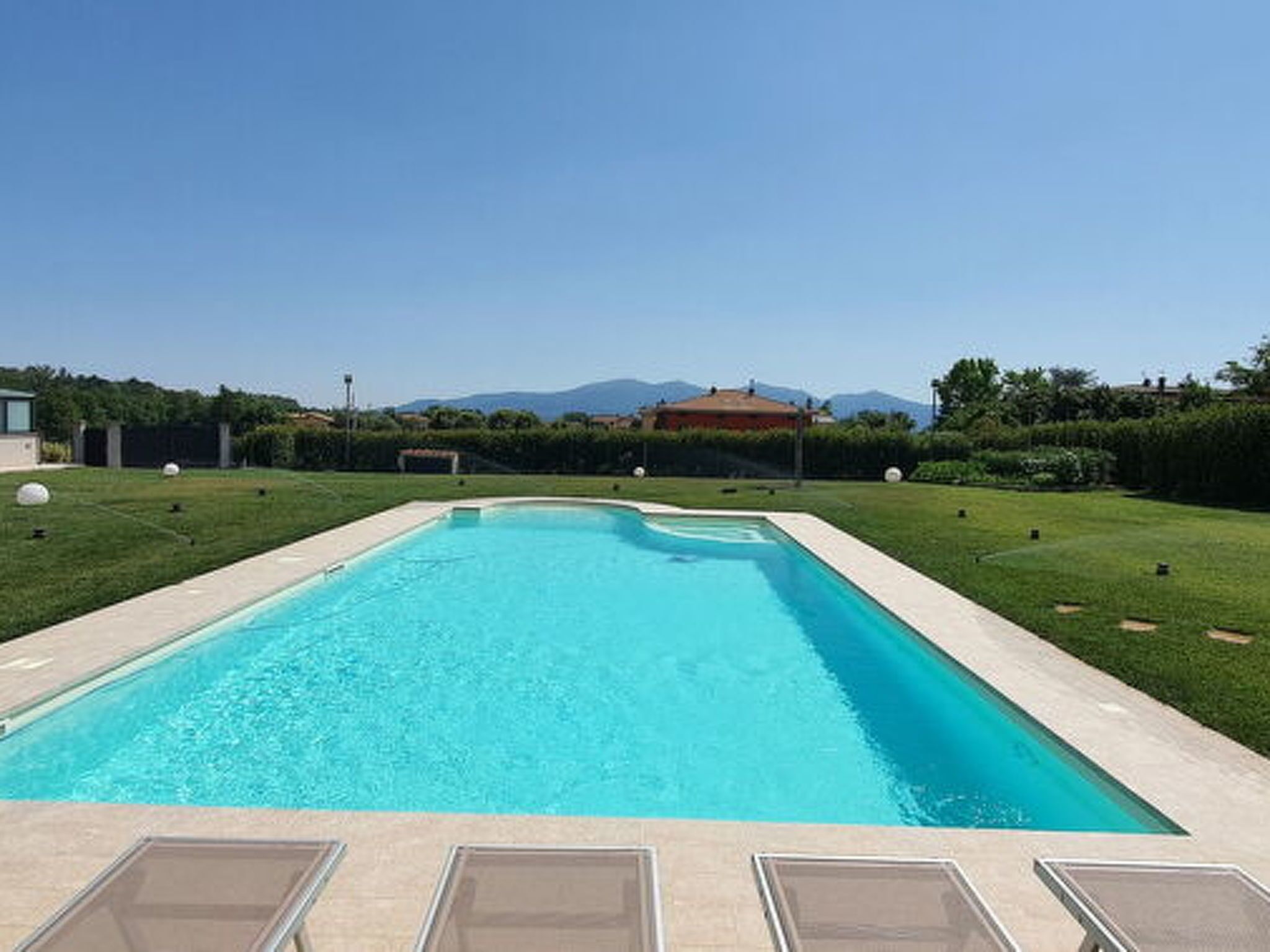 A rectangular swimming pool with a clear blue water, surrounded by a well-maintained lawn and a hedge.