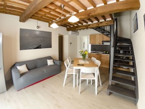 A modern interior with a sofa, dining table, chairs, a staircase, and kitchen area. - Tenuta Il Giardino Proprietà by Interhome (Capannori)