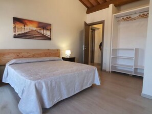A bedroom with a bed, a nightstand, a painting, a wardrobe, and a door leading to another room. - Tenuta Il Giardino Proprietà by Interhome (Capannori)