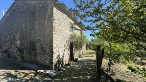 Ein Steinhaus mit geneigtem Dach, einer kleinen Tür und einem von Bäumen gesäumten, eingezäunten Bereich.