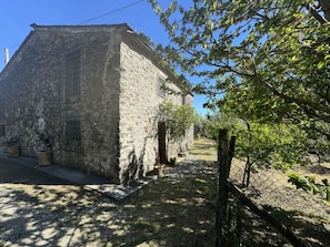 A stone building with a sloped roof, a small door, and a fenced area with trees. - Il Cantuccio Proprietà by Interhome (Colognora)
