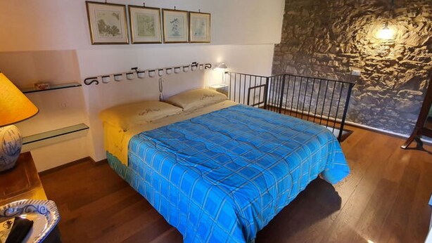Ein Schlafzimmer mit einem Bett, einem Nachttisch, einer Lampe und einer Steinwand.