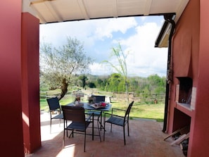 An outdoor patio with a table and chairs, a brick floor, and a view of a green landscape with trees and hills. - Ai Salici by Interhome (Lari)