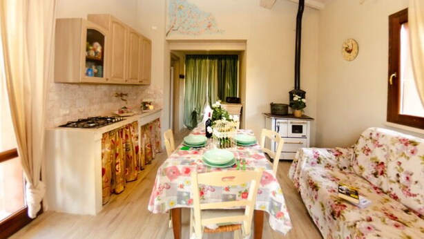 A cozy kitchen with a dining table set for four, a sofa, and a wood-burning stove. - Ai Salici by Interhome (Lari)