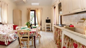 A room with a dining table, chairs, a television, and a kitchen area with cabinets and a sink. - Ai Salici by Interhome (Lari)