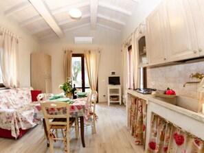 A room with a dining table, chairs, a television, and a kitchen area with cabinets and a sink. - Ai Salici by Interhome (Lari)