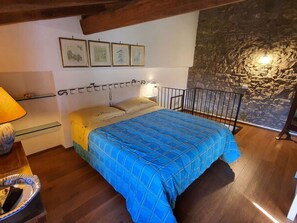 Een slaapkamer met een bed, nachtkastje, lamp en een stenen muur.