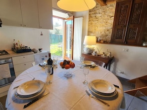 Ein Esszimmer mit gedecktem Tisch, Geschirr, Besteck und einer Obstschale. Im Hintergrund eine Steinsäule und Holzsärchen.