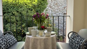 Un balcón con una mesa para dos personas, un florero y una pared de piedra al fondo.