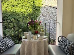 Ein Balkon mit Tisch für zwei Personen, einem Blumenstrauß und einer Steinmauer im Hintergrund.
