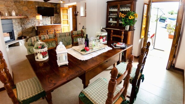 Zona pranzo con tavolo in legno, sedie, divano e parete in pietra.
