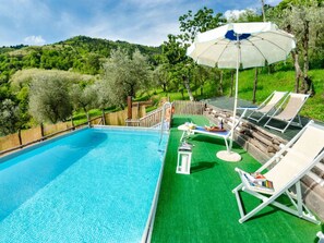 Ein Schwimmbecken mit Holzterrasse, Liegestühlen und Sonnenschirm.