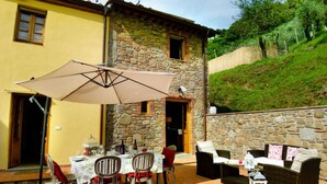 Un patio esterno con tavolo e sedie, un divano in vimini e un muro in pietra.