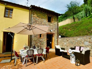 Eine Terrasse im Freien mit Tisch, Stühlen, einer Korbsessel-Couch und einer Steinwand.
