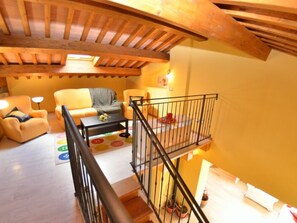 A loft-style living room with a wooden ceiling, a sofa, a coffee table, and a staircase with a railing. - Borgo Di Zacco by Interhome (La Sassa)