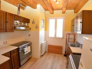 A kitchen with wooden cabinets, a stove, a radiator, and a window. - Borgo Di Zacco by Interhome (La Sassa)