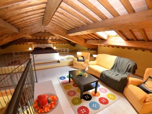 Une chambre aménagée dans les combles, avec un plafond en bois, un lit, un canapé, une table basse et un tapis coloré orné de motifs en forme de boutons.