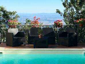 A poolside area with wicker furniture and potted plants, overlooking a scenic view. - Borgo Di Zacco by Interhome (La Sassa)