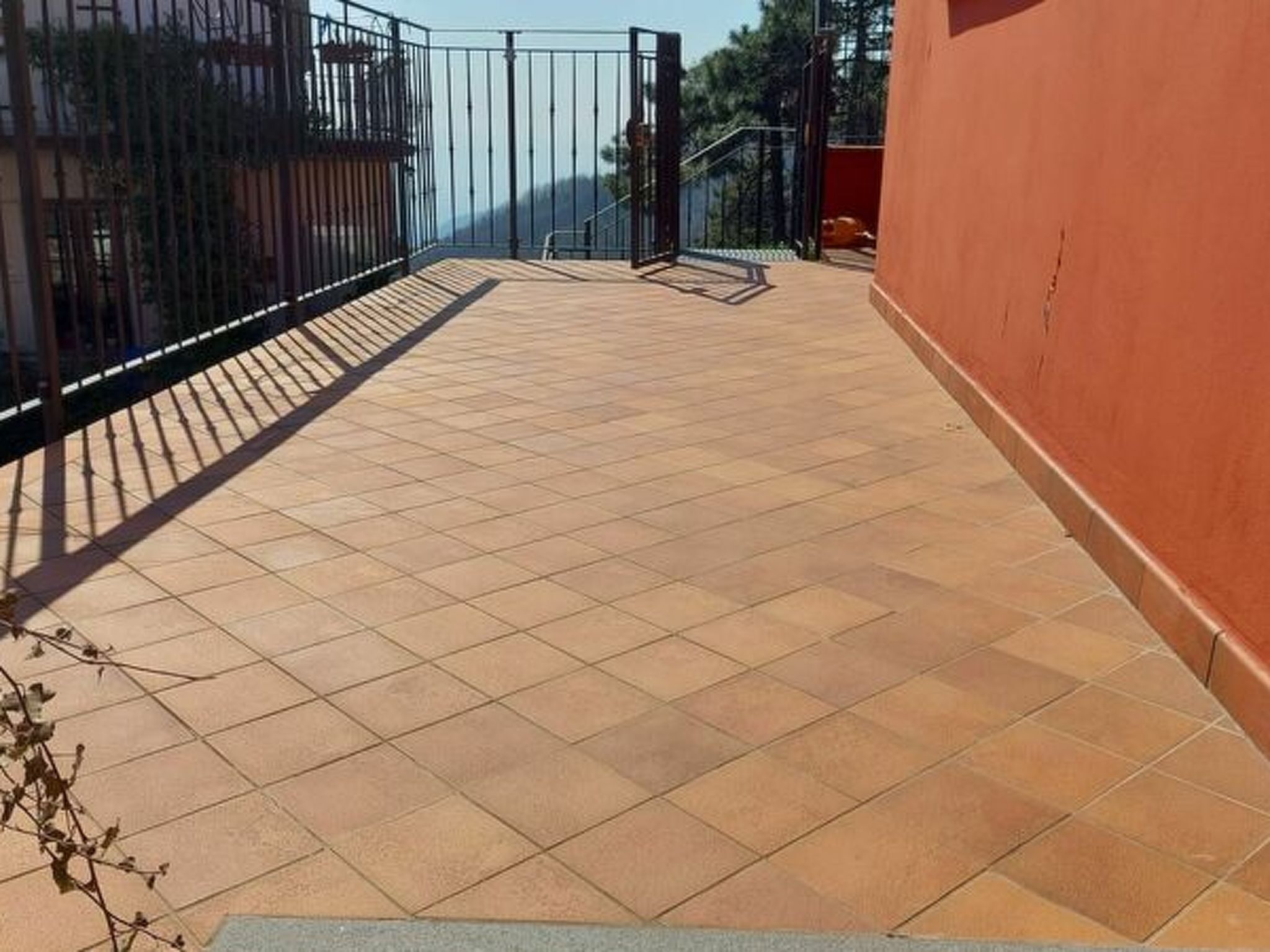 A tiled balcony with a metal railing, a red wall, and a clear sky in the background.
