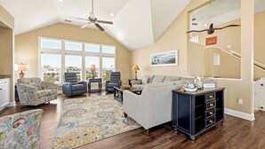 A spacious living room with a high ceiling, large windows, a ceiling fan, and a view of the outside. - Seabreeze at Ocean Hill: New to Rental Program, Private Pool & Hot Tub, Dog-Friendly (Corolla)