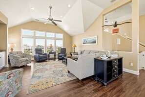A spacious living room with a high ceiling, large windows, a ceiling fan, and a view of the outside. - Seabreeze at Ocean Hill: New to Rental Program, Private Pool & Hot Tub, Dog-Friendly (Corolla)
