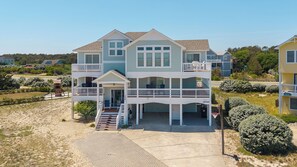 A two-story beachfront house with a balcony, a covered porch, and a driveway leading to the entrance. - Seabreeze at Ocean Hill: New to Rental Program, Private Pool & Hot Tub, Dog-Friendly (Corolla)