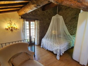 A bedroom with a wooden ceiling, a bed with a white canopy, a chair, a wall-mounted light fixture, and a window. - Il Cantuccio by Interhome (Colognora)