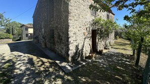 Ein Steinhaus mit kleinem Eingang, umgeben von einer Schotterauffahrt und Bäumen.