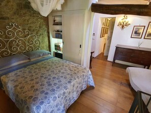 Une chambre à coucher avec une couvre-lit à motifs, une tête de lit en bois, une table de chevet avec des livres et une commode avec un miroir.