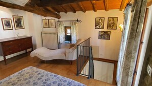 Ein Schlafzimmer mit Bett, Kommode, Stuhl und einer Treppe sowie Blick ins Freie.