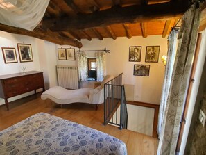 Ein Schlafzimmer mit Bett, Kommode, Stuhl und einer Treppe sowie Blick ins Freie.