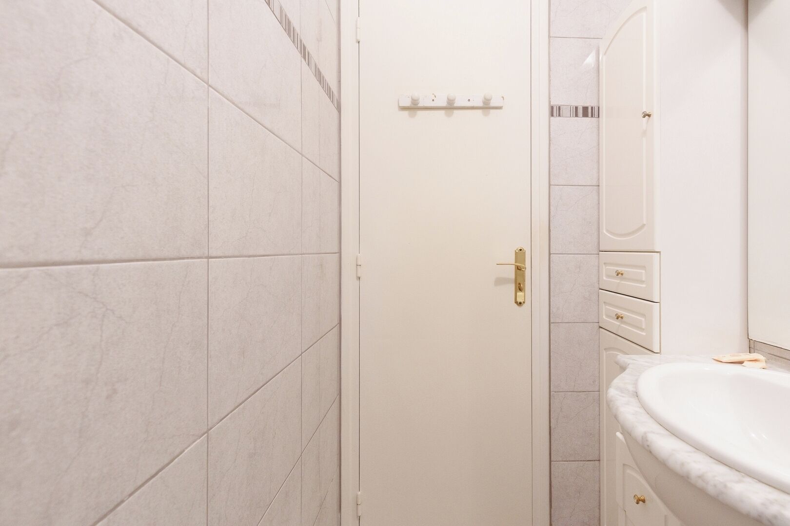 A bathroom with white tiles, a white sink, and a gold door handle.