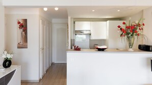 A modern kitchen with white cabinets, a central island, and a vase of red flowers. - Upstays Bright 1BR 50m² with terrace Cannes center (Cannes)