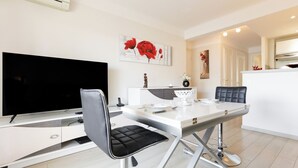 A modern kitchen with a dining area, a flat-screen TV, and a white dining table with chairs. - Upstays Bright 1BR 50m² with terrace Cannes center (Cannes)