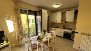 Une cuisine compacte avec des meubles blancs, une table à manger avec des chaises, une petite télévision et un balcon avec vue.