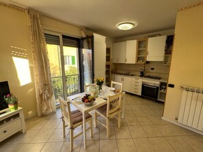 Eine kompakte Küche mit weißen Schränken, einem Esstisch mit Stühlen, einem kleinen Fernseher und einem Balkon mit Blick.