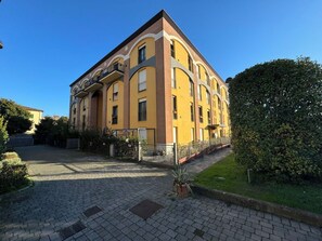 Ein mehrstöckiges Gebäude mit gelber Fassade, einem gepflasterten Auffahrtsweg und einem gepflegten Rasen.