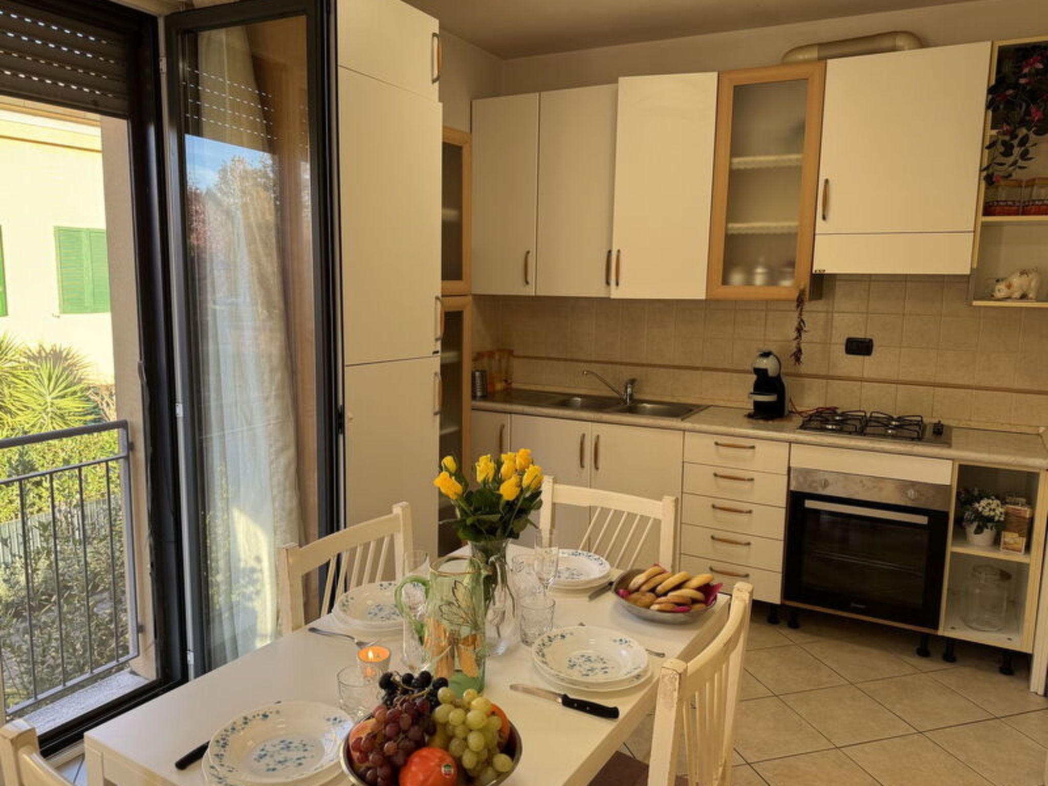 A kitchen with white cabinets, a dining table set with plates, a vase of flowers, and a fruit bowl.