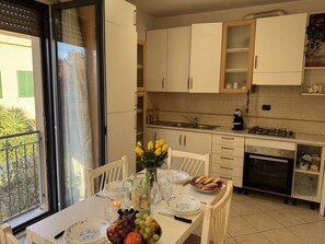 Et køkken med hvide skabe, et spisebord dækket med tallerkener, en vase med blomster og en skål med frugt.