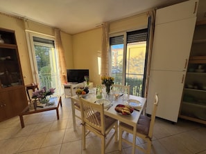 A dining area with a table set for two, a television, and a balcony with curtains. - Al Civico 80 by Interhome (Ciciana)