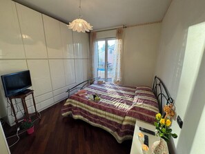 Ein Schlafzimmer mit einem Bett, einem Fernseher auf einem Tisch, einem Fenster mit Vorhängen und einer Topfpflanze.